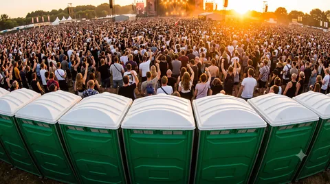 Row of green event toilets in front of a large festival crowd at a main stage